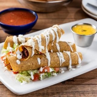Chicken Flautas: Crispy, hand-rolled corn tortillas filled with chicken tinga. Topped with a lime crema drizzle & served with a side of pico de gallo and queso.