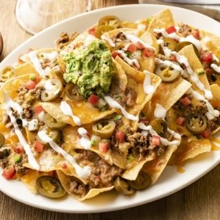 Stacked Nachos: Chips piled high with seasoned ground beef, refried beans and queso. Topped with lime crema, pico de gallo, pickled jalapeños and guacamole.