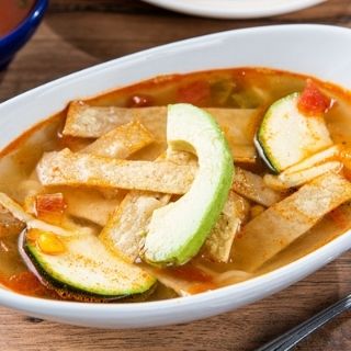 Chicken Tortilla Soup: Homemade chicken broth loaded with chicken tinga, rice, zucchini and Jack cheese, topped with fresh avocado and tortilla strips.
