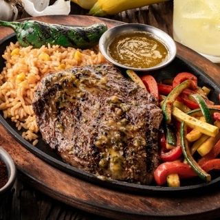 Carne Asada: A 9 oz. marinated and seasoned mesquite-grilled steak served on a skillet with seasoned butter, sautéed vegetables and Mexican rice.