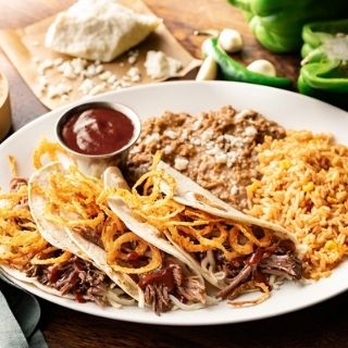 Brisket Tacos: Shredded beef brisket, Jack cheese, fried onion strings and jalapeño-BBQ sauce in warm, hand-pressed flour tortillas. Served with Mexican rice and choice of beans.