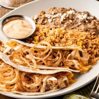 Southwest Chicken Tacos: Mesquite-grilled chicken, cheddar cheese, creamy red chile sauce and fried onion strings in warm, hand-pressed flour tortillas. Served with Mexican rice and choice of beans.